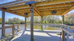 Une terrasse en bois agrémentée d’une pergola, de deux ventilateurs, d’un panneau indicateur et offrant une vue sur une étendue d’eau.