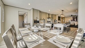 A modern kitchen with wooden cabinets, stainless steel appliances, and a dining area with a long table set for four. - Cozy Hillside Retreat Near Dale Hollow Lake! (Burkesville)