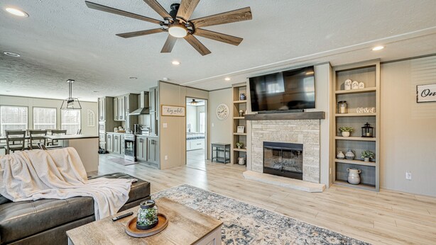 A spacious living area with a fireplace, a ceiling fan, and a kitchen in the background. - Cozy Hillside Retreat Near Dale Hollow Lake! (Burkesville)