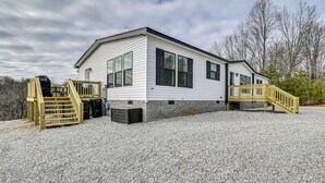 A single-story mobile home with a gravel driveway, wooden deck, and a small staircase leading to a deck area. - Cozy Hillside Retreat Near Dale Hollow Lake! (Burkesville)