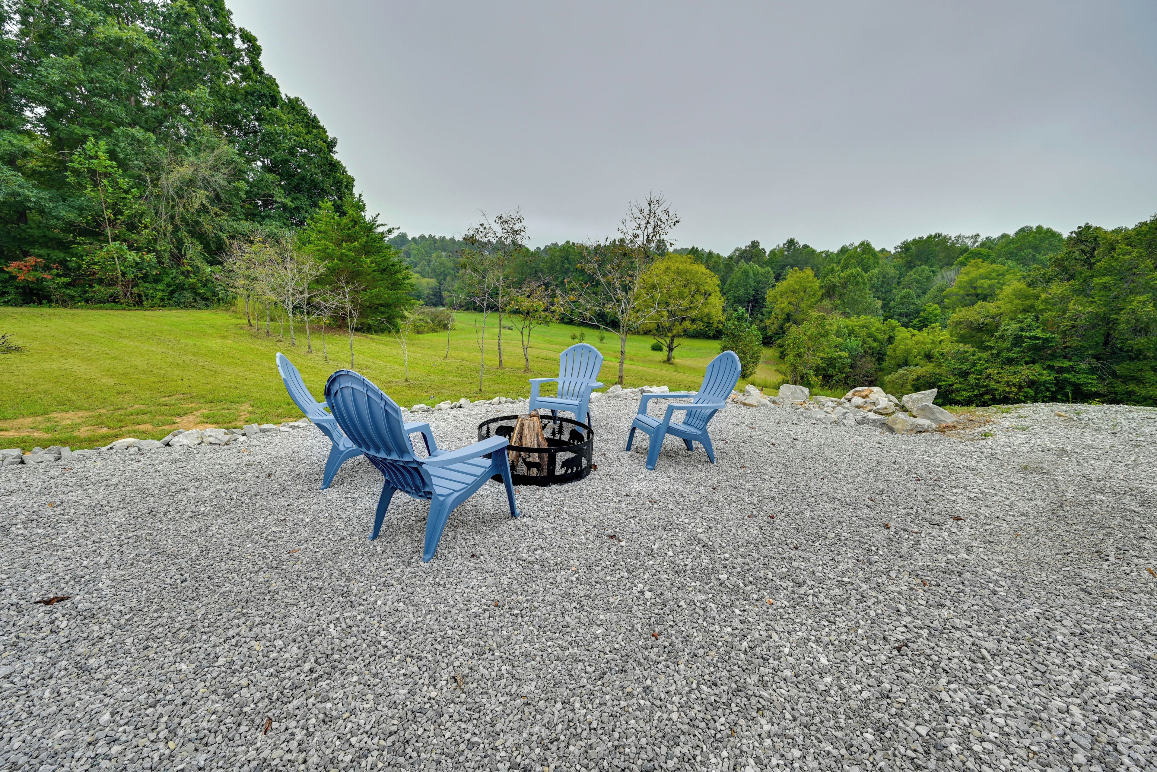 A gravel area with four blue Adirondack chairs arranged around a central fire pit.