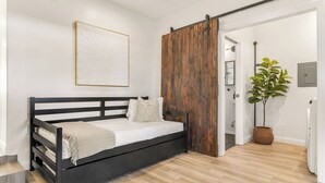 A bedroom with a bed, a wooden sliding door, a potted plant, and a white wall with a framed picture. - Hot Tub BBQ Island Outdoor Living Near San Diego Beaches Glidden Glow by Avantstay (San Diego)