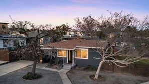 A residential house with a dark exterior, a visible front door, and a small front yard with a tree and a planter. - Hot Tub BBQ Island Outdoor Living Near San Diego Beaches Glidden Glow by Avantstay (San Diego)