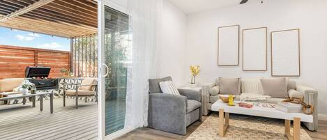 A modern living room with a grey sofa, a coffee table, and a balcony with a barbecue grill.