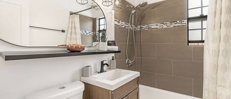 Un baño moderno con inodoro, lavamanos, tocador, ducha y espejo.