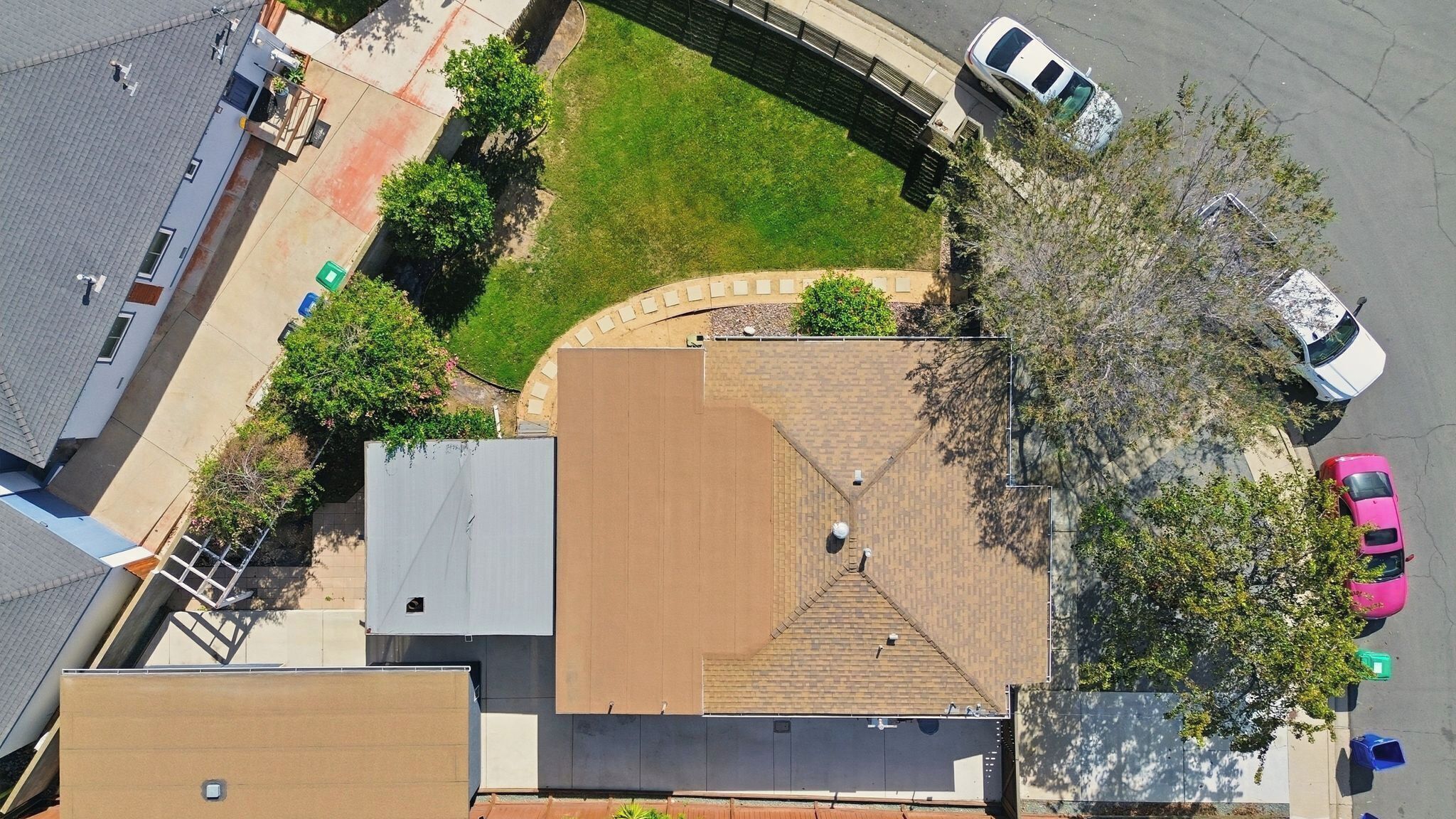 An aerial view of a residential area with a house featuring a sloped roof, a paved driveway, and a small lawn.