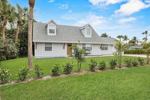 A two-story house with a grey roof, white siding, and a front door. There are small shrubs in front of the house and a lawn. - Deck + Pool Table! Walk to Dtwn Jensen Beach (Jensen Beach)