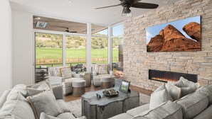 Un salón amplio con chimenea de piedra, asientos cómodos y un gran ventanal con vistas a un campo de golf.