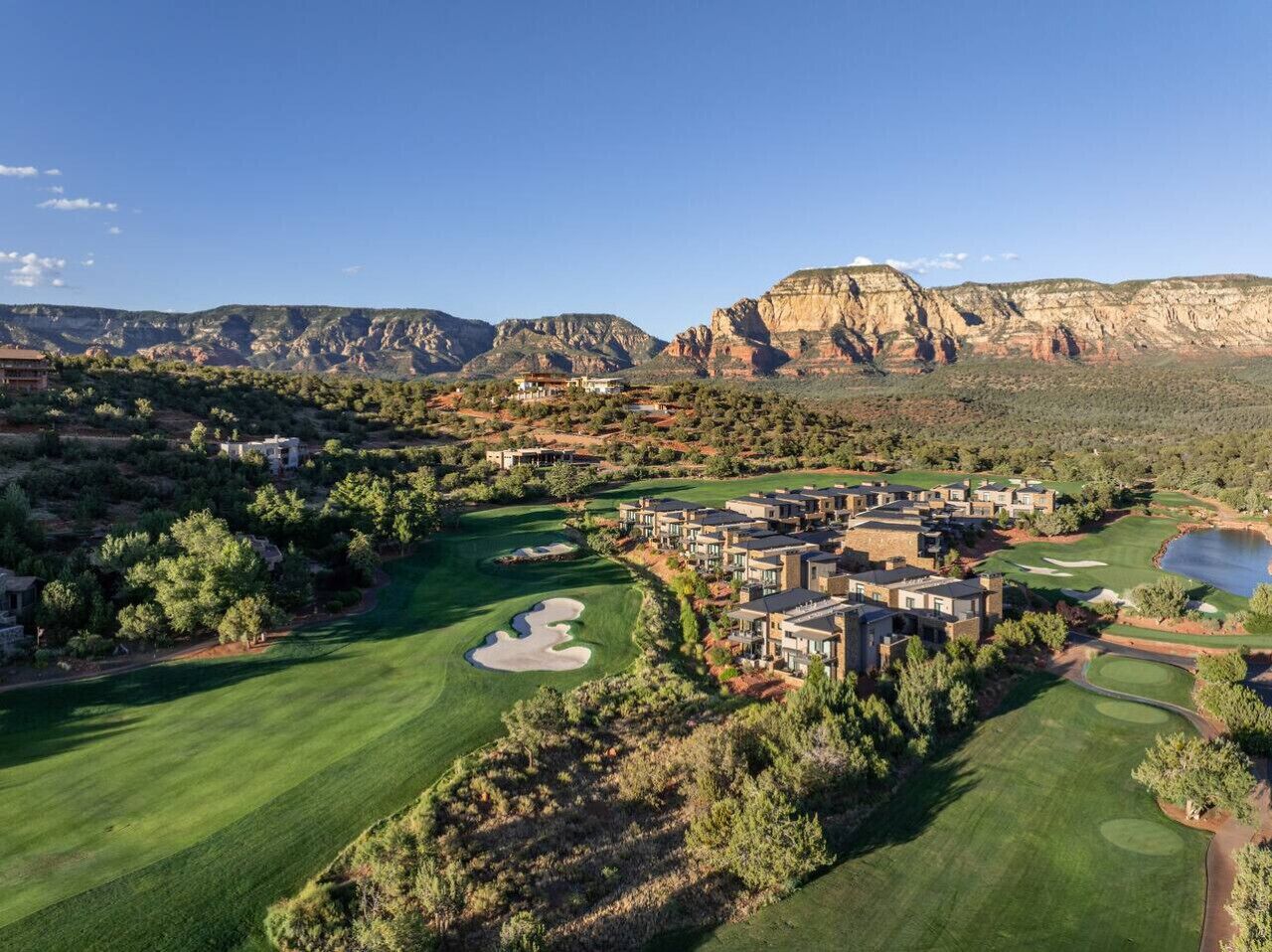 A golf course with a clubhouse and residential buildings, surrounded by mountains and greenery.