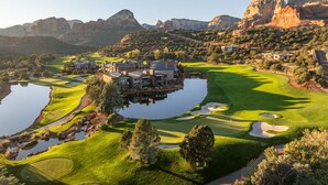 Un campo de golf con un club de campo, un estanque y montañas circundantes.