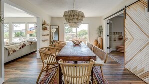 Ein geräumiger Essbereich mit Holztisch, Korbstühlen, einer Chandelüster und Blick ins Freie.