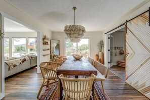 Ein geräumiger Essbereich mit Holztisch, Korbstühlen, einer Chandelüster und Blick ins Freie.