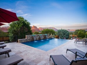 A swimming pool with a waterfall feature, surrounded by lounge chairs and a stone deck. - 5.5k Sqft Luxury Home with Large Suites, Views, Hot Tub & Firepit (Sedona)