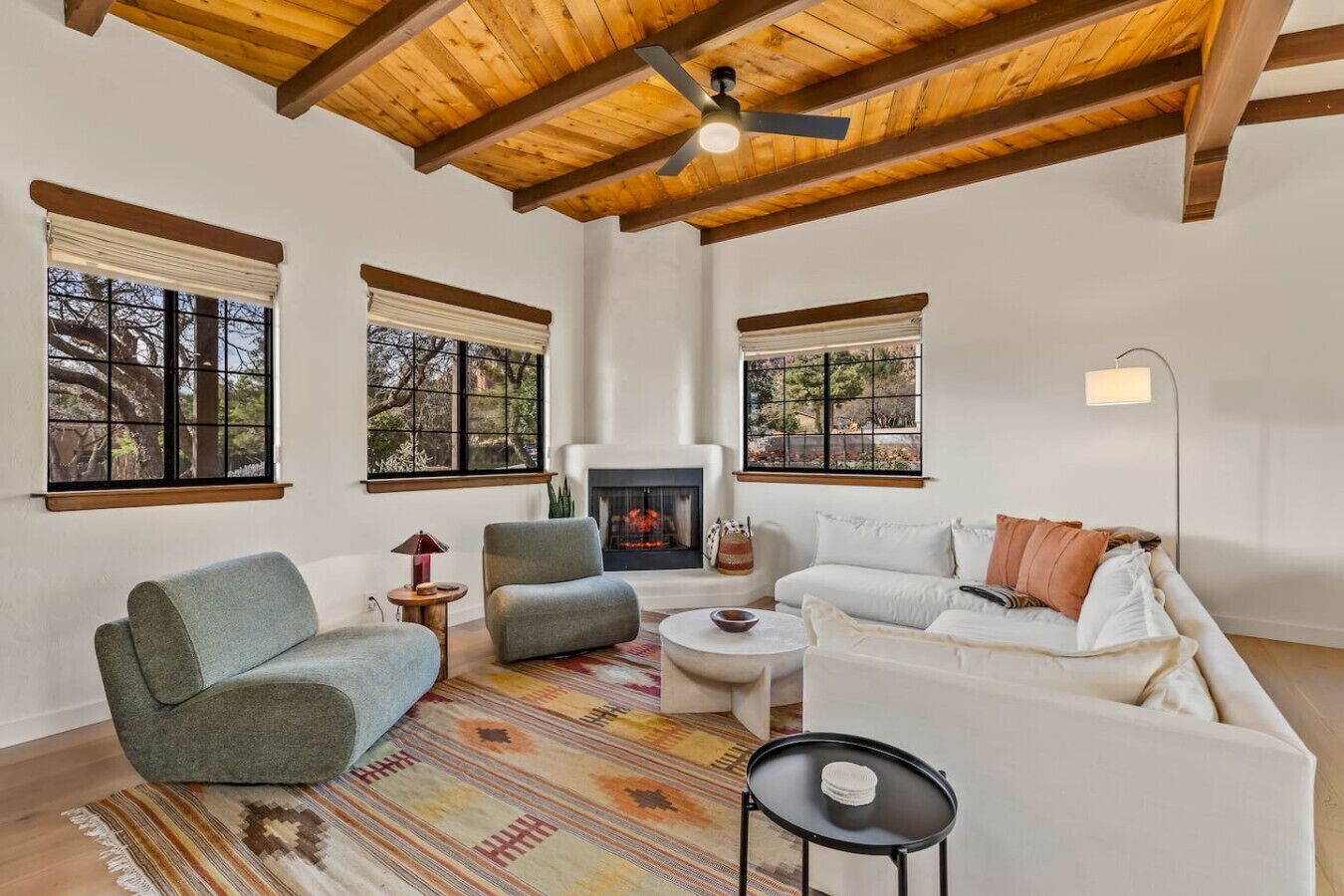 A spacious living room with a fireplace, large windows, and a ceiling fan.