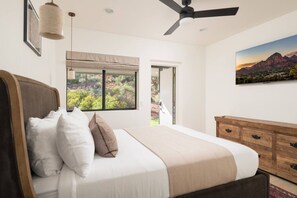 Ein Schlafzimmer mit Bett, Deckenventilator, Fenster mit Blick ins Grüne und einem Holzschrank.