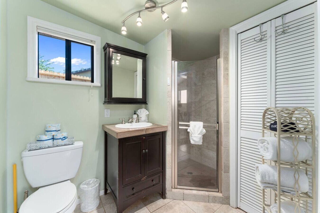 A bathroom with a toilet, sink, mirror, shower, and towel rack.