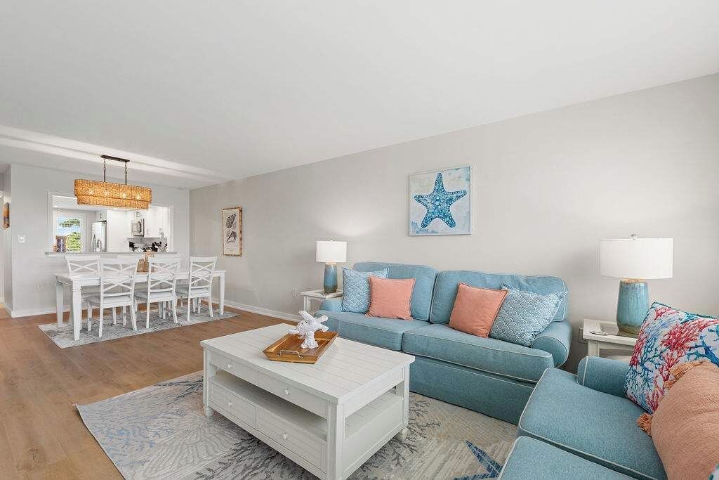 A modern living room with a white coffee table, a blue sofa, and a dining area with white chairs.