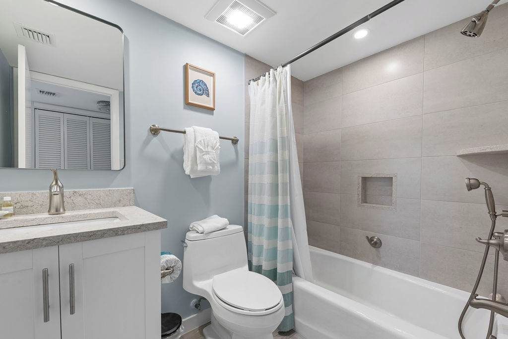 A bathroom with a toilet, sink, mirror, shower, and a towel rack.