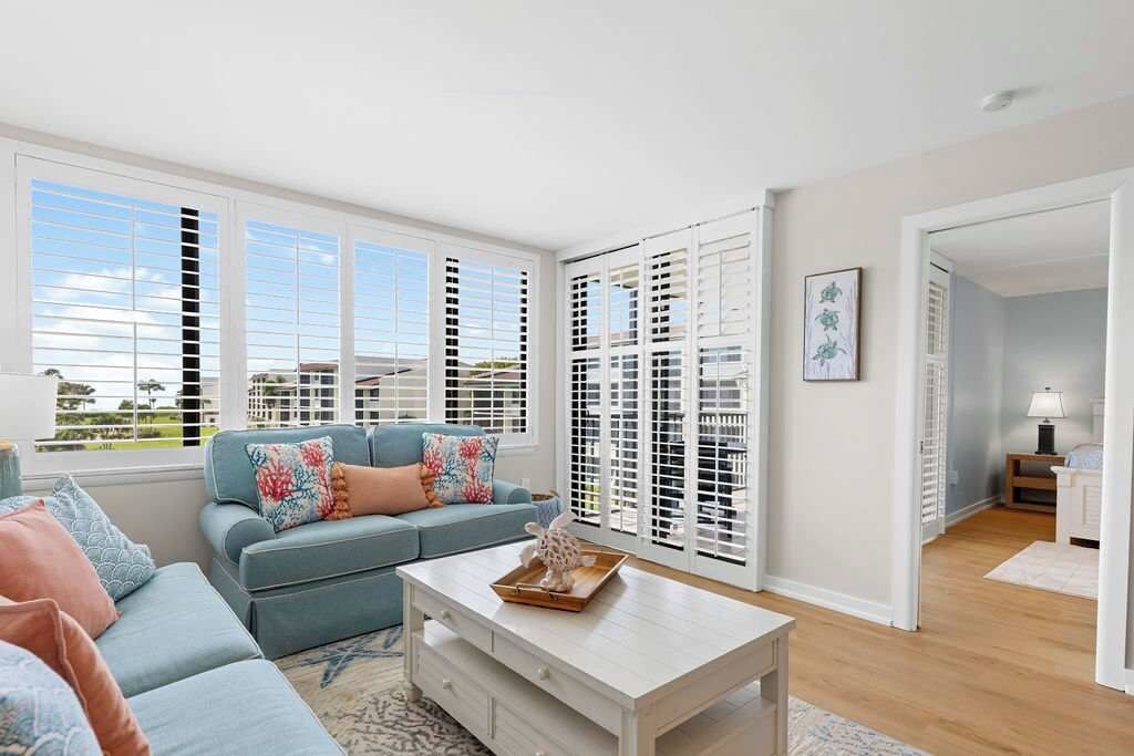 A living room with a sofa, a coffee table, and a view through a window with blinds.