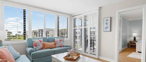 A living room with a sofa, a coffee table, and a view through a window with blinds.