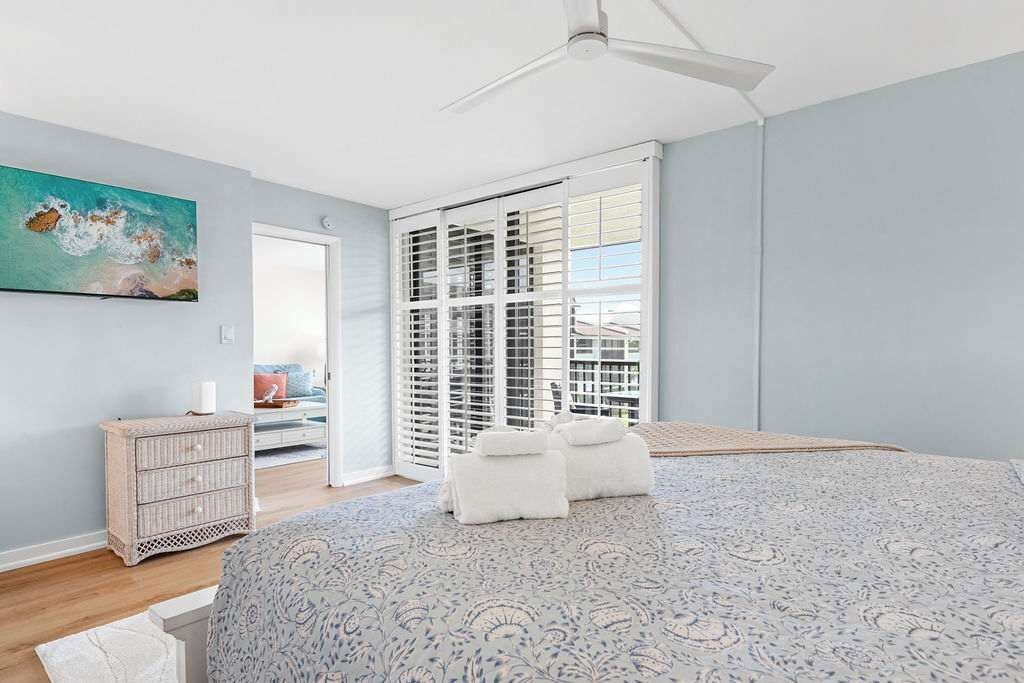 A bedroom with a bed, a ceiling fan, a window with blinds, a painting on the wall, and a dresser.