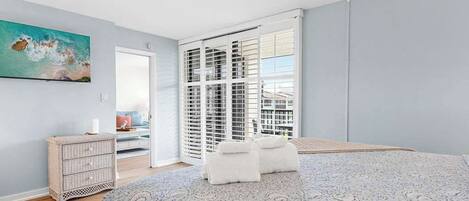 A bedroom with a bed, a ceiling fan, a window with blinds, a painting on the wall, and a dresser.