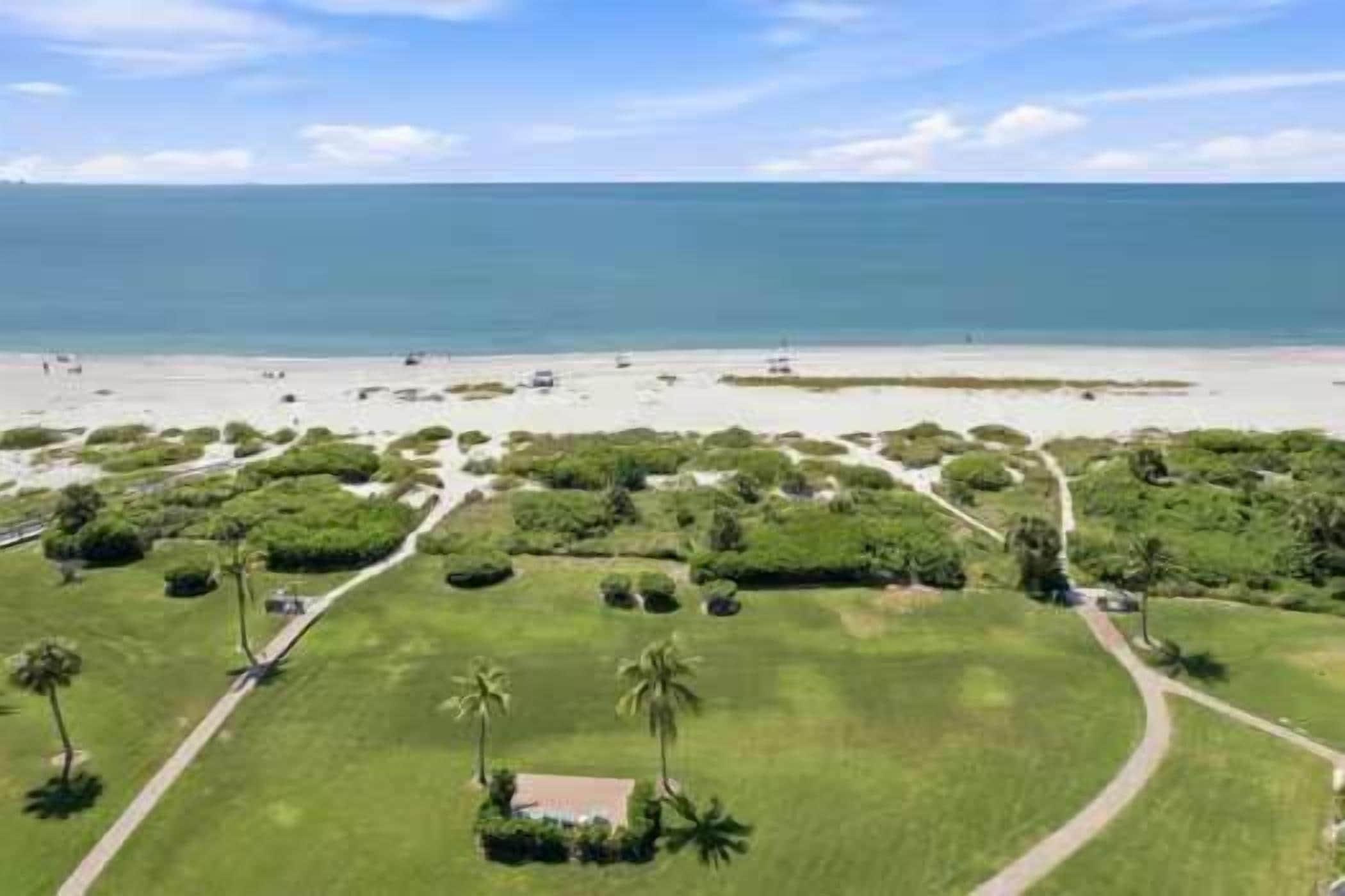 An aerial view of a coastal property with a beach, green lawns, and a clear sky.
