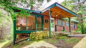 Une cabane rustique avec des fondations en pierre, de grandes fenêtres et une véranda couverte.