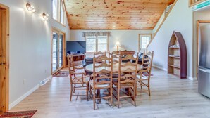 Un grand espace à manger avec une table et des chaises en bois, une cuisine équipée d’un réfrigérateur et un espace en mezzanine avec un plafond en bois.