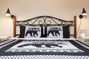 A bed with a black metal headboard, two pillows with bear designs, and a quilt with a bear and forest pattern.