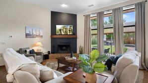 Ein Wohnzimmer mit Kamin, einer Couch, einem Couchtisch und einem großen Fenster mit Vorhängen.