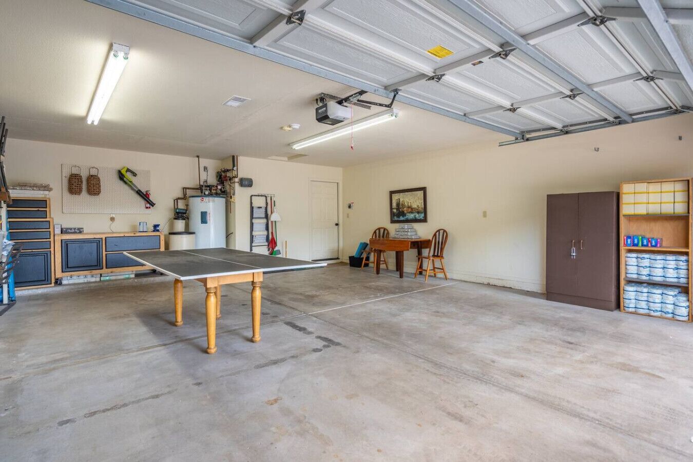 A spacious garage with a ping pong table, a workbench, and a water heater.