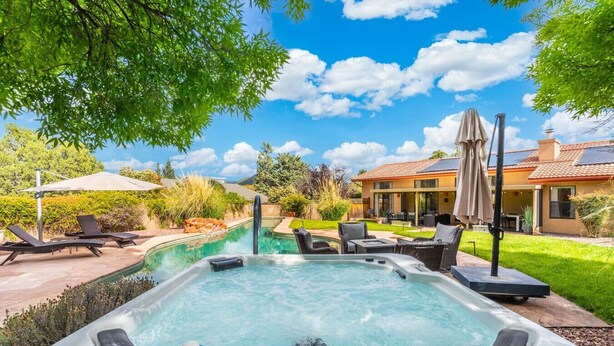 Ein Whirlpool im Garten mit einem Pool, Liegestühlen und einem Haus im Hintergrund.