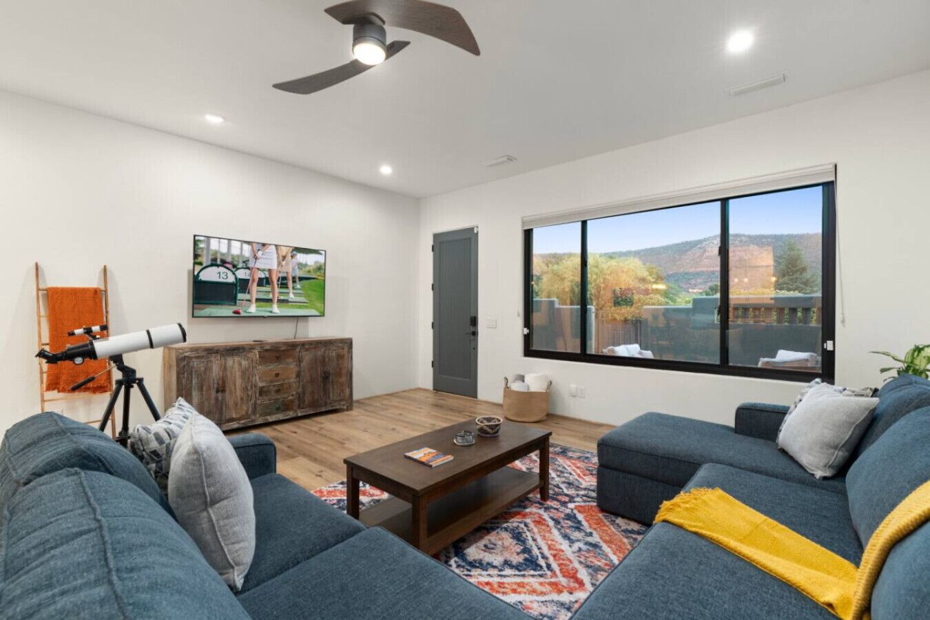 A modern living room with a large window, a ceiling fan, a telescope, and a television.