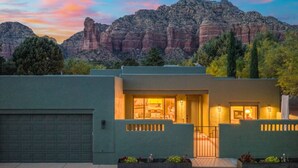 Una casa moderna con garaje, un acceso bien iluminado y vistas a formaciones rocosas rojas al fondo.