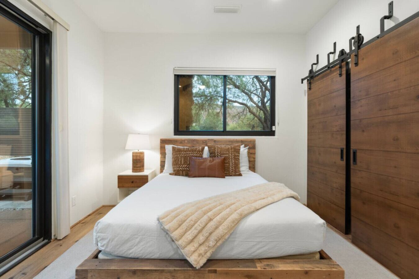 A bedroom with a large bed, a nightstand, a window with a view of trees, and a wooden wardrobe.