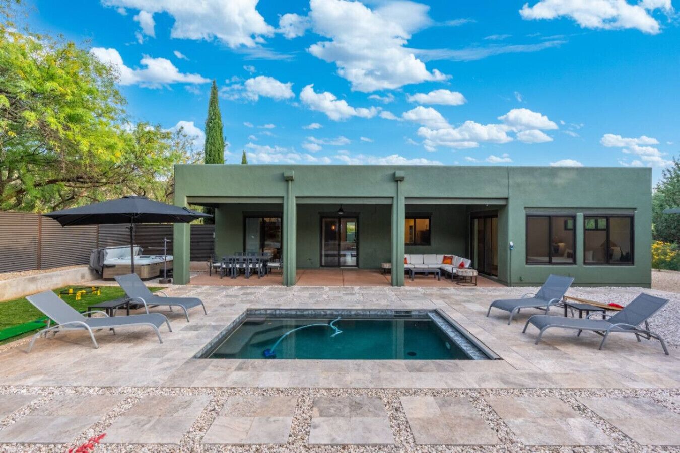 A modern outdoor pool area with lounge chairs, a hot tub, and a covered patio.