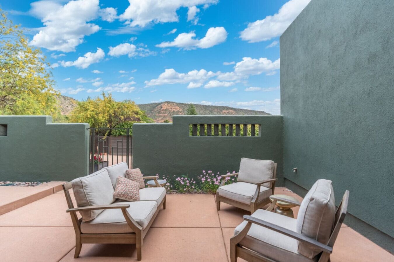 An outdoor patio with two sofas and a table, surrounded by a low wall and a gate.