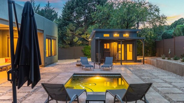 Un patio moderno al aire libre con piscina, zona de estar y estructura cubierta.
