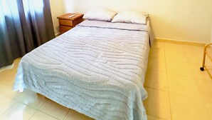 Quarto com cama, mesa de cabeceira, ar condicionado e cortina.