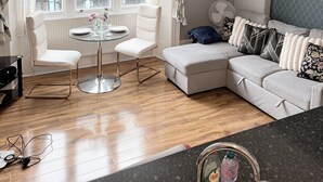 Una sala moderna con una mesa de comedor de vidrio, sillas blancas, un sofá gris y una lámpara colgante negra.