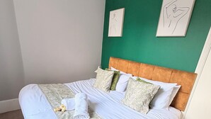 Una cama bien hecha con un cabecero verde, ropa de cama blanca y dos obras de arte en la pared.