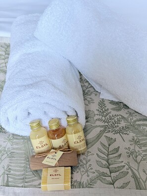 Ordentlich angeordnete Pflegeprodukte auf einem Bett mit einem blumigem Bettbezug.