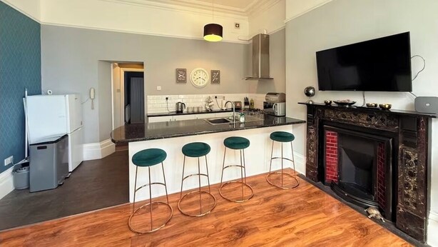 Una cocina moderna con una isla central, taburetes de bar, un televisor de pantalla plana y una chimenea.