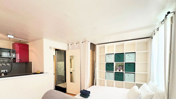 Ein kleines Hotelzimmer mit Küchenzeile, einem Bett mit Kissen, einer Schlafcouch und einem eingebauten Stauraum mit Schubladen.