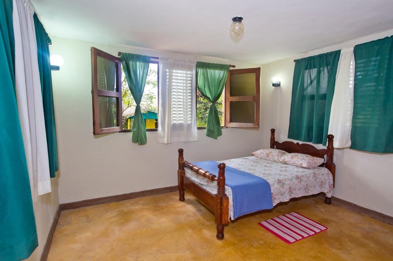 A bedroom with a wooden bed, green curtains, and a window with blinds.