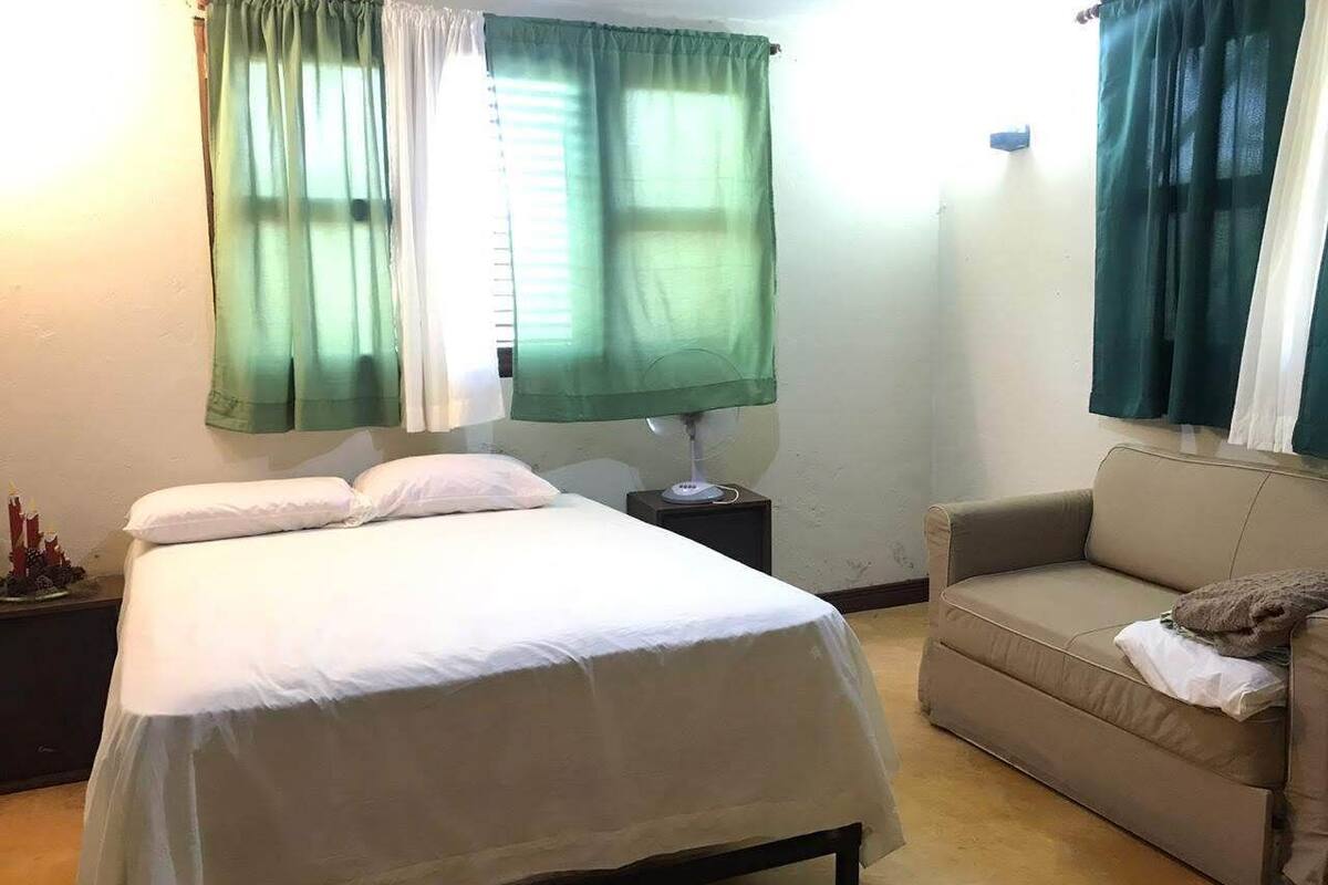 Un dormitorio con cama, mesita de noche, lámpara, sofá y cortinas.
