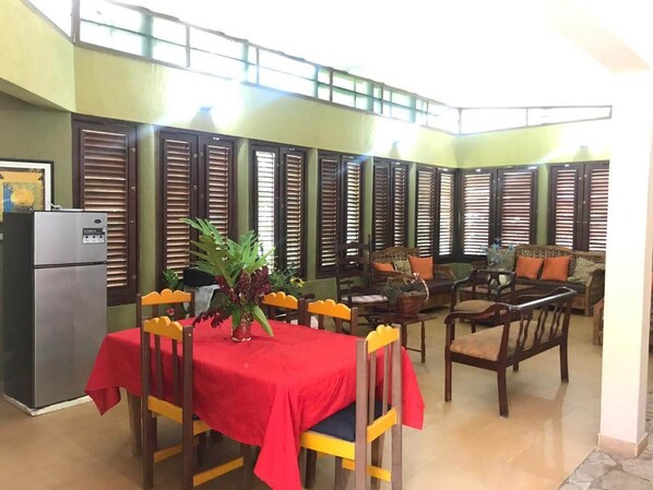 A dining area with a red tablecloth, wooden chairs, and a refrigerator.