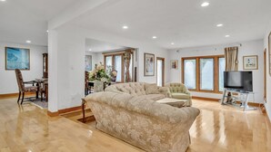 A spacious living room with a large beige sectional sofa, a television on a stand, and a dining area with a table and chairs. - Spacious, Quiet, 4BR+office, 1.5 acres yard (Lincoln)