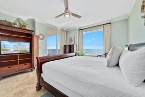 A spacious bedroom with a large bed, a television on a wooden stand, and a view of the ocean through the window. - Beach Front Indigo Condo A Week in Paradise Perdido Key Florida (Pensacola)